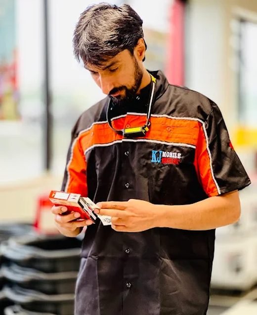KJ, the mechanic who comes out to your vehicle, in a KJ Mobile Mechanic shirt checking a part.